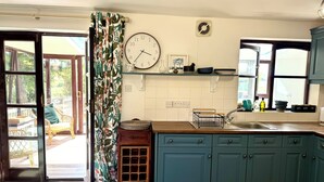 Cozinha com armários verde-água, bancada de madeira, relógio e janela com vista para o verde.