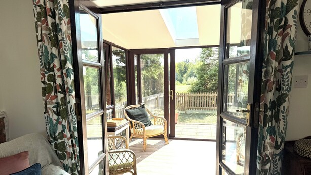 Quarto com porta de vidro deslizante que dá para um pátio externo com deck de madeira, mobiliário de vime e vista para um jardim.