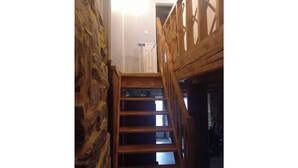 Una escalera de madera con un muro de piedra a un lado, que conduce a una habitación con una cama y un ventanal.