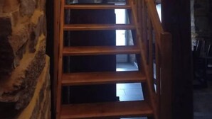 Eine Holztreppe mit einer Steinsäule an der Seite führt zu einem Zimmer mit einem Bett und einem Fenster.