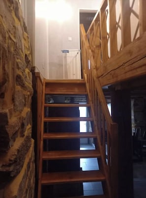 Un escalier en bois, avec un mur en pierre d’un côté, mène à une pièce qui contient un lit et une fenêtre.