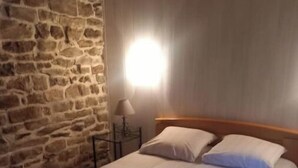 Una cama bien hecha con ropa de cama y toallas blancas, un cabecero de madera y una pared de piedra.
