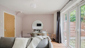 Un salón moderno con un sofá gris, un espejo redondo, una mesa de comedor con sillas y un ventanal corredero que da a un jardín.