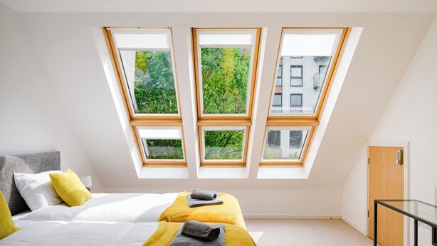 Un dormitorio con una cama, dos ventanas, una puerta y una mesita.