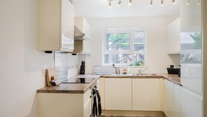 Una cocina moderna con armarios blancos, encimera de madera, estufa integrada y una ventana con vistas a árboles.