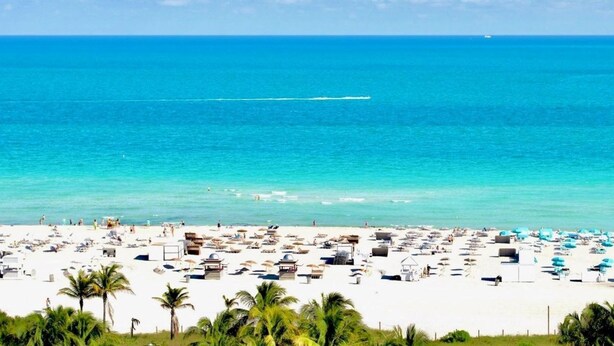 A beach with numerous sun loungers and umbrellas, a clear blue sky, and the ocean in the background. - Oceanside 2 bedroom Escape with Pool, Steps from the Beach - (Miami Beach)
