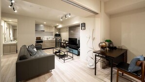 A modern living room with a sofa, coffee table, and dining area. There is a kitchen in the background with a microwave and stove. - Mondomio Sapporo 207 (Sapporo)