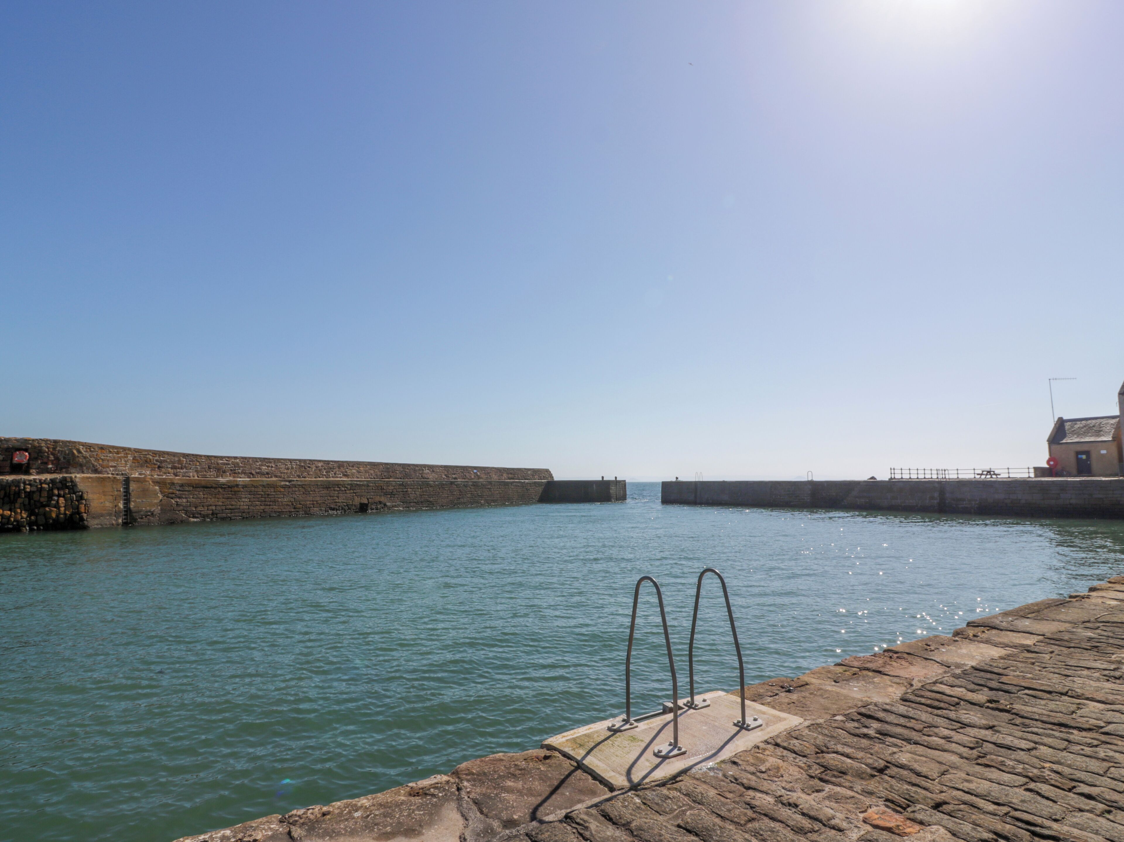 A waterfront with a stone wall and a metal railing by the water.