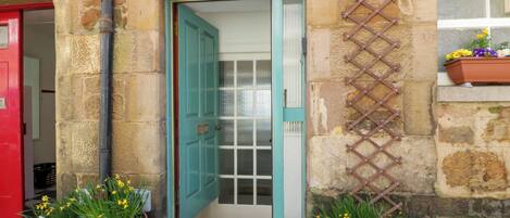 A stone building with a teal door, potted plants, and a lattice on the wall.
