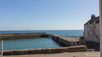 A coastal view with a stone quay, a clear sky, and a building with a red door.