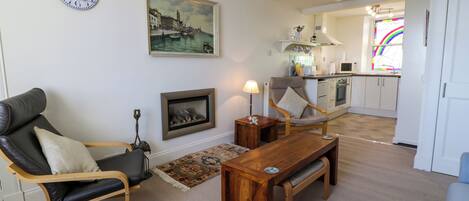 Una sala de estar con un sofá, una mesa de centro de madera, una silla, una chimenea y una cocina al fondo.