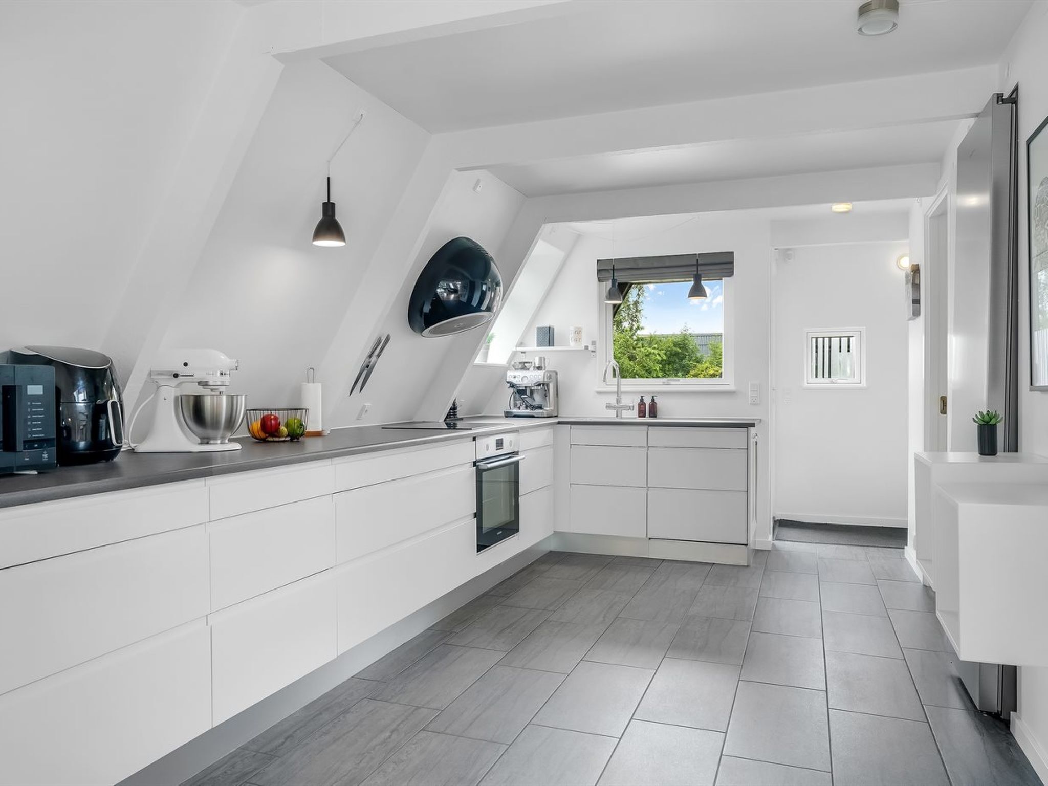 A modern kitchen with white cabinetry, a built-in oven, and a coffee machine.