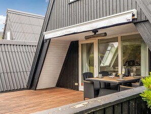 A modern house with a wooden deck, a glass door leading to a dining area with a table and chairs, and a grey metal roof. - "Ernstine" by Interhome (Farsø)