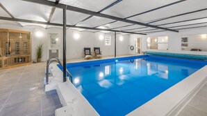 Piscina interna com água azul, área de sauna e espaço de descanso com cadeiras.