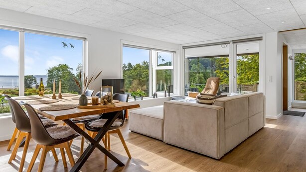 A modern living room with a dining area, large windows, and a view of the outdoors.