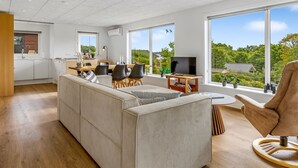 A modern living room with a large sectional sofa, a dining area, and a TV on a wooden stand.