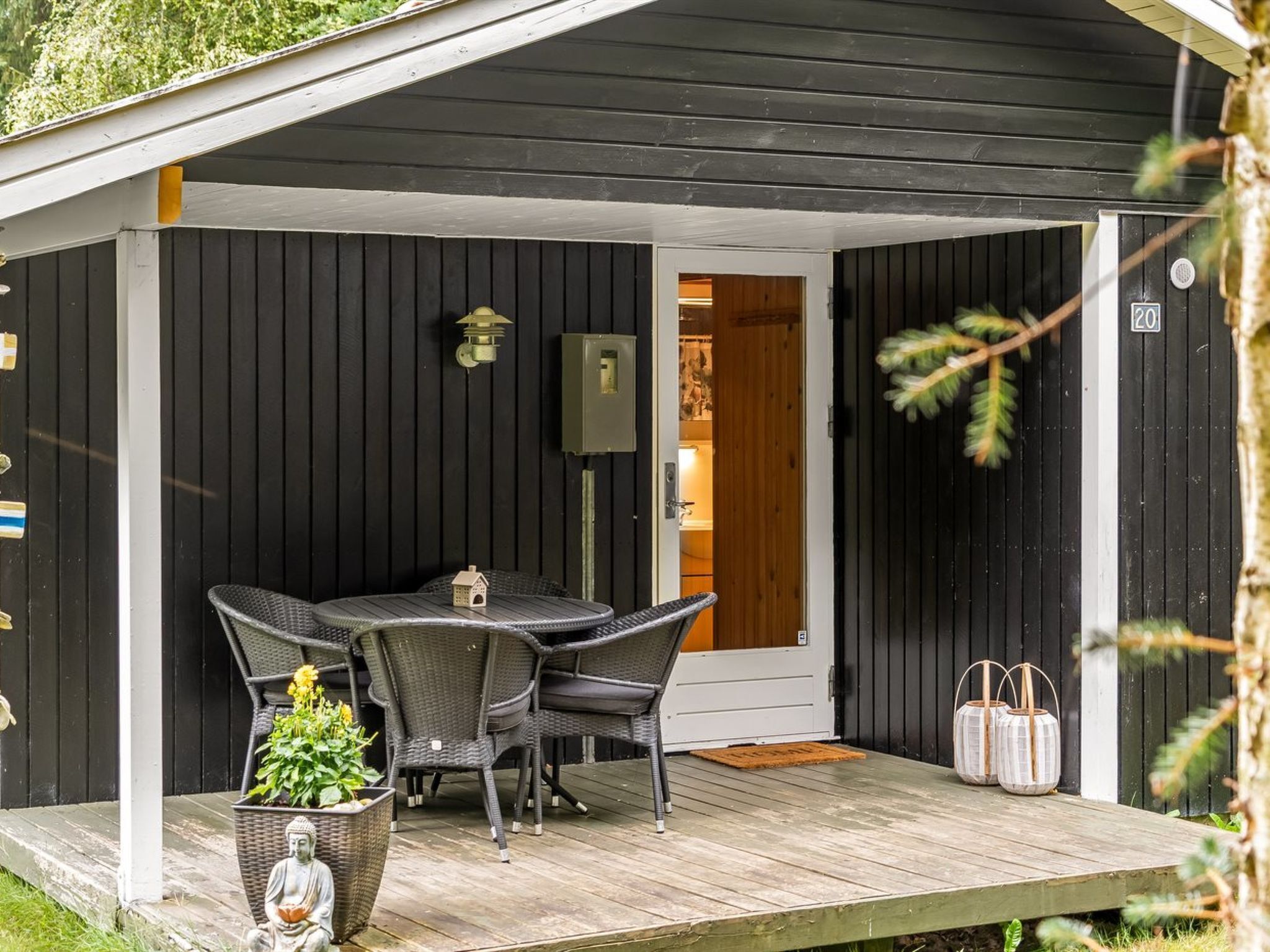 Een overdekt terras met een tafel, stoelen, een klein Boeddhabeeldje en een potplant.