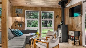 Ein gemütliches Cabin-Interieur mit Holzbalkendecke, einer Couch, einem Esstisch mit Stühlen, einem Fernseher und einem Kamin.