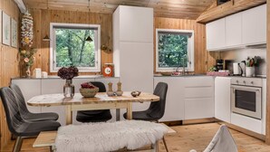 Eine moderne Küche mit Holzschränken, ein Essbereich mit einem weißen Tisch und Stühlen sowie Blick auf Grünflächen durch die Fenster.