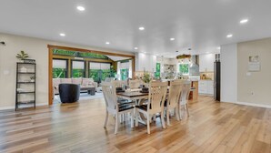 Una cocina amplia con electrodomésticos modernos, un comedor con sillas de madera y un amplio ventanal con vistas a la vegetación.