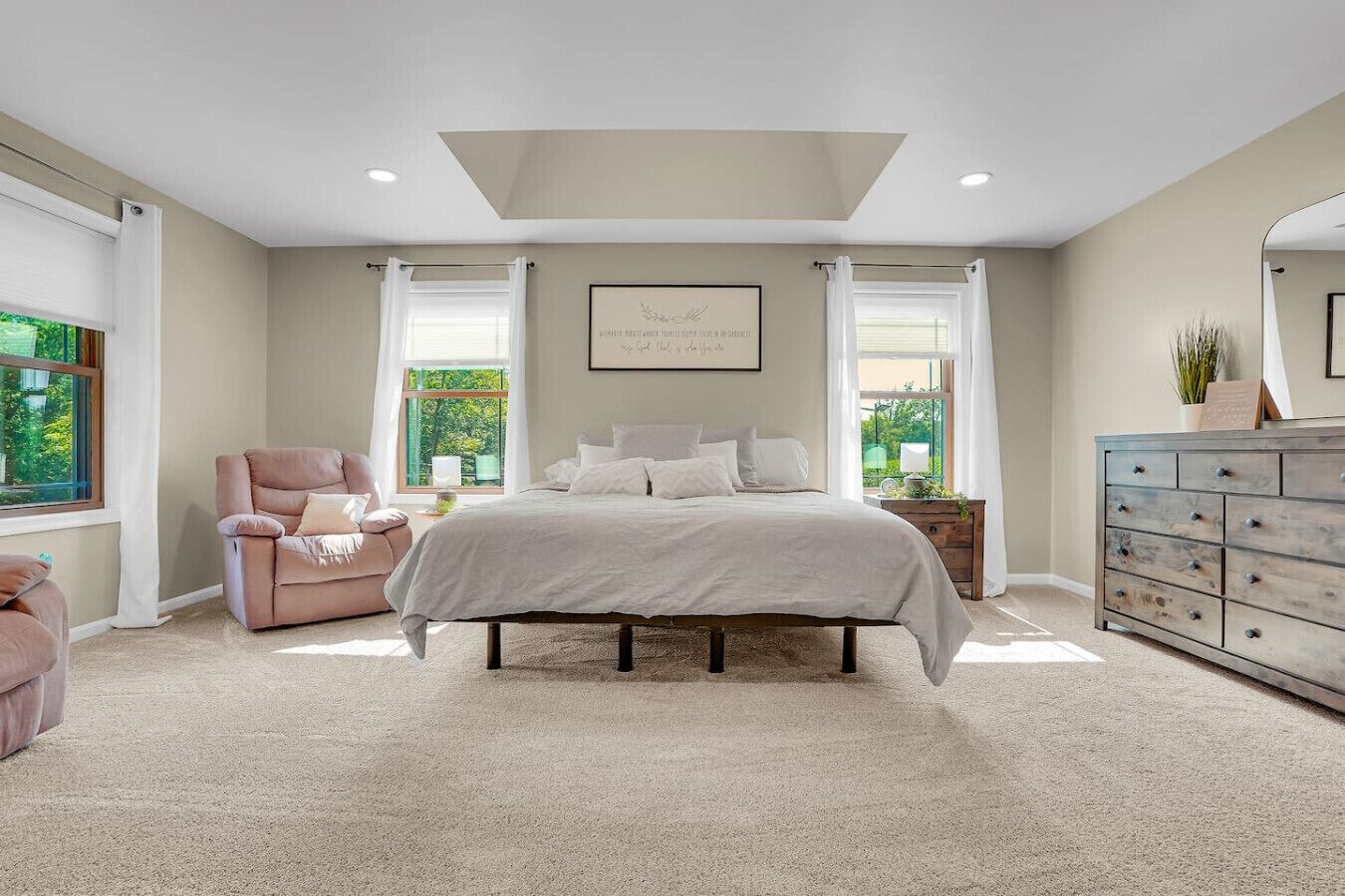 Une chambre à coucher avec un grand lit, une chaise, une commode et une fenêtre avec des rideaux.