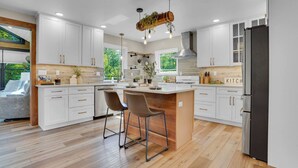 Una cocina moderna con armarios blancos, una isla central con taburetes, un refrigerador negro y una lámpara de techo de madera.