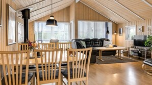 A spacious loft with a high ceiling, wooden walls, a black leather sofa, a dining area with wooden chairs, and a TV in the living area.