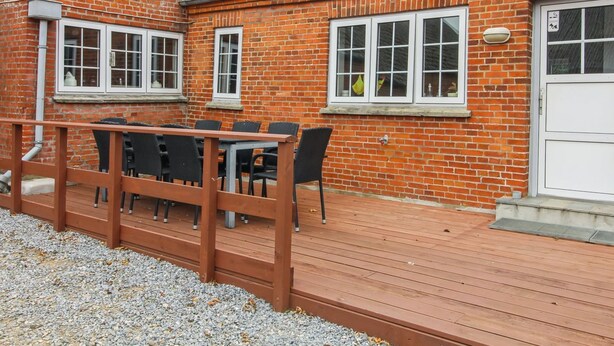 Ein Backsteinhaus mit einer Holzterrasse, einem Tisch und Stühlen sowie einer weißen Tür.