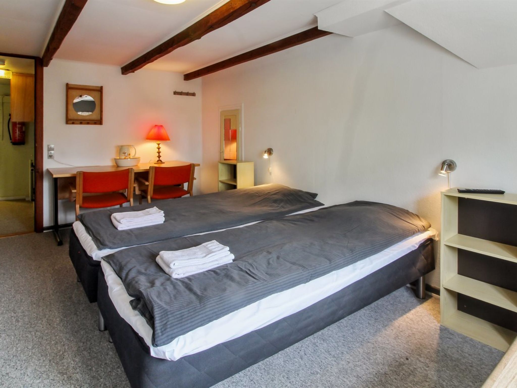 A bedroom with two beds, a desk, a chair, a lamp, and a shelf.