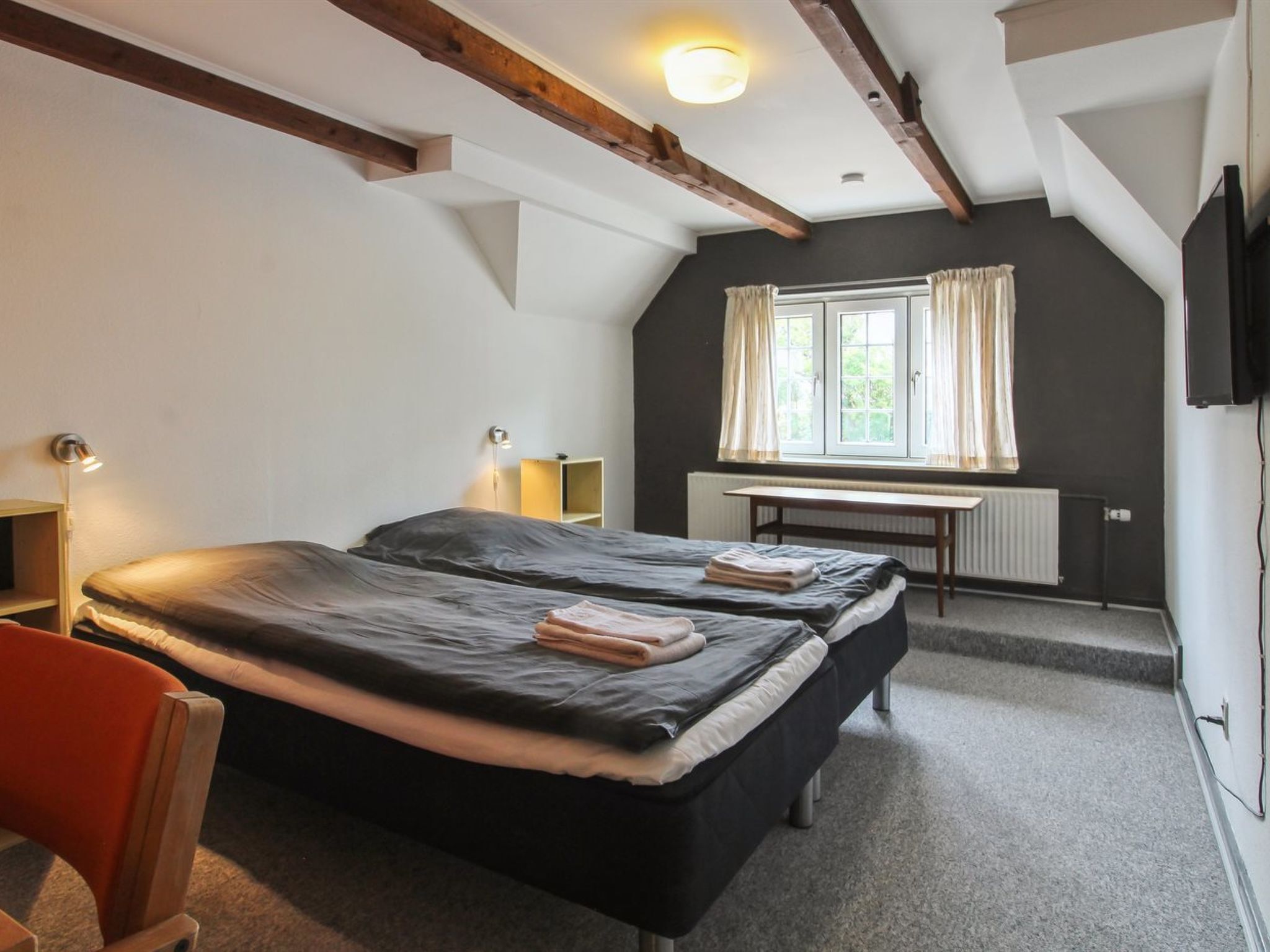 Ein Zimmer mit zwei Betten, einem Schreibtisch, einem Stuhl, einem Heizkörper und einem Fernseher.