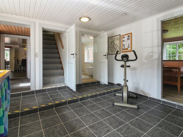 Un intérieur moderne avec un escalier menant à une autre pièce, un vélo d’exercice fixé au mur et un sol carrelé.