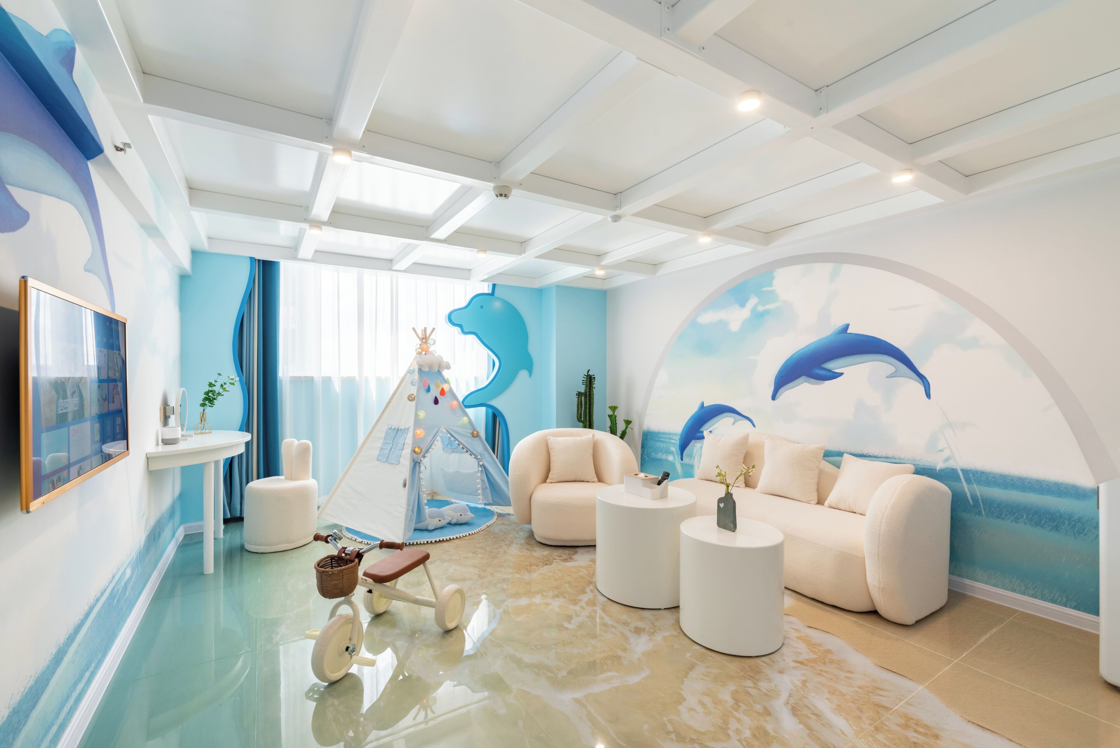A modern living room with a white sofa, round coffee tables, a tent, and a dolphin mural on the wall.