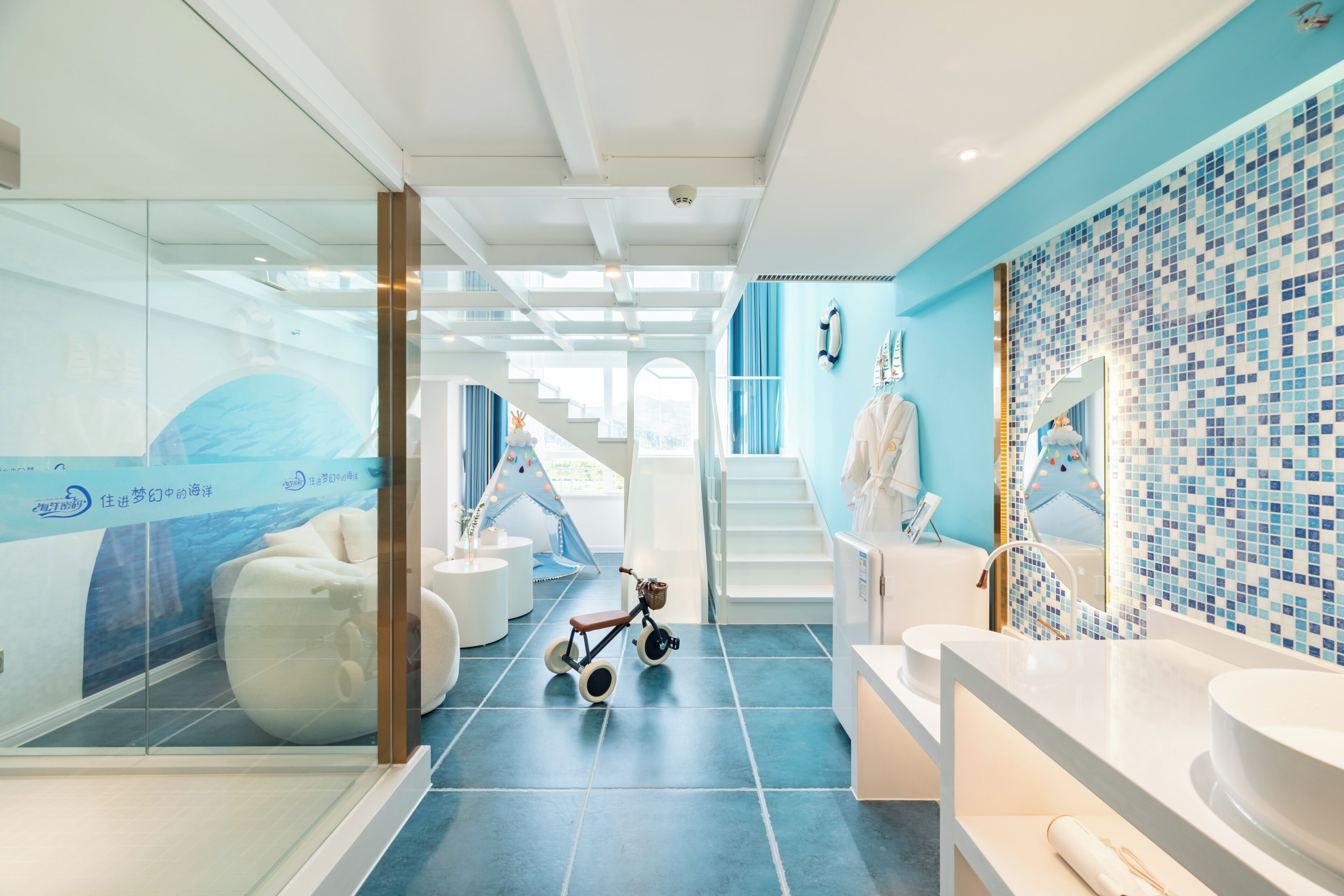Un baño moderno con piso de azulejos azules, sanitarios blancos y una bicicleta infantil.