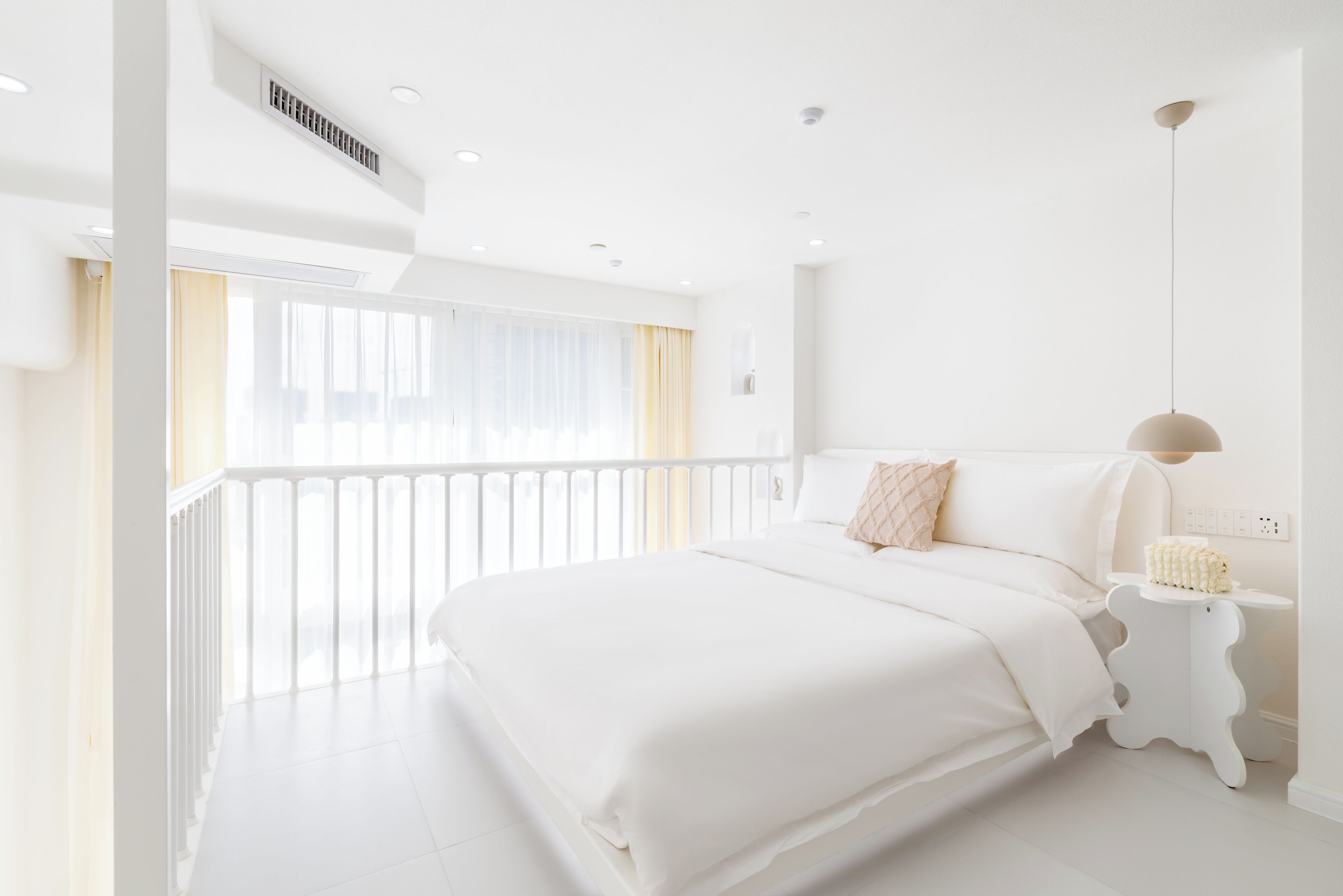 A modern hotel room with a large bed, a bedside table, and a view of the outdoors.