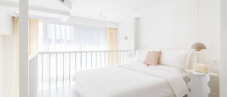 A modern hotel room with a large bed, a bedside table, and a view of the outdoors.