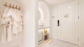 A hotel room with a white robe rack, a refrigerator, slippers, and a door with a sign.