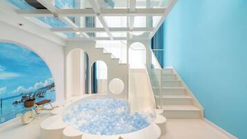 A modern interior with a ball pit, a staircase, and a mural of a beach scene.