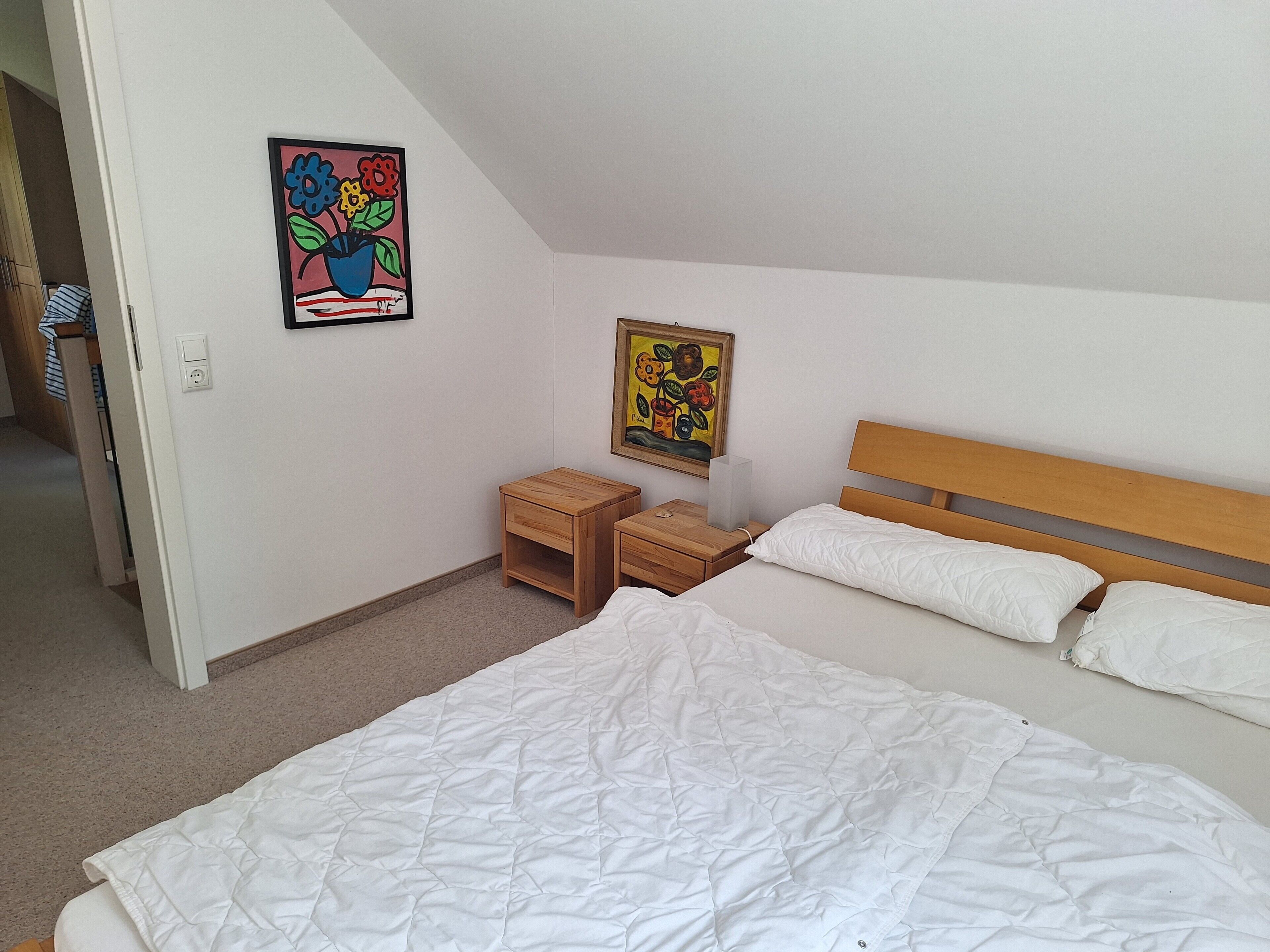 Un dormitorio con cama, mesitas de noche y dos cuadros colgados en la pared.