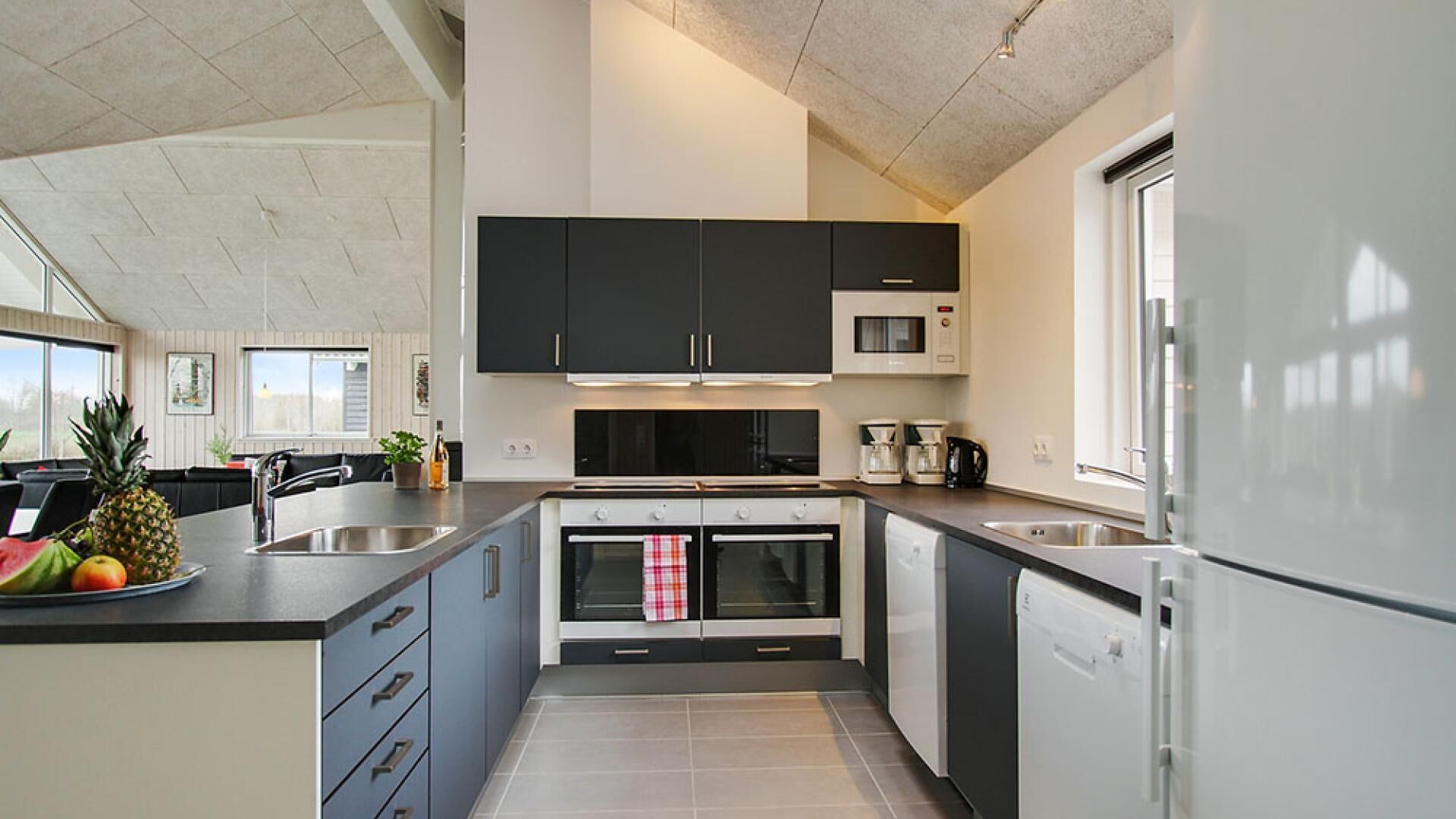 Una cocina moderna con armarios oscuros, un microondas, un refrigerador y un comedor con una mesa y sillas.