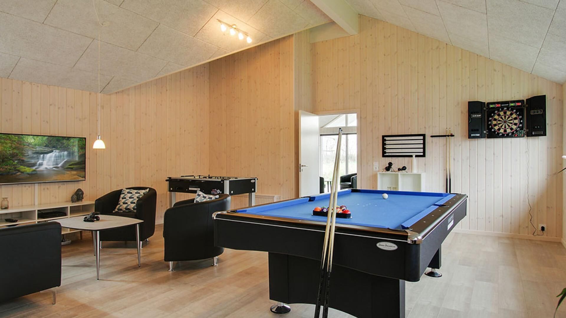A room with a pool table, a dartboard, and a television displaying a nature scene.