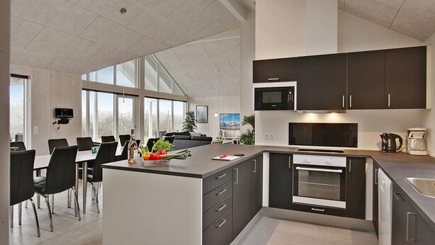 Una cocina moderna con una isla central, electrodomésticos integrados y un comedor con un amplio ventanal.