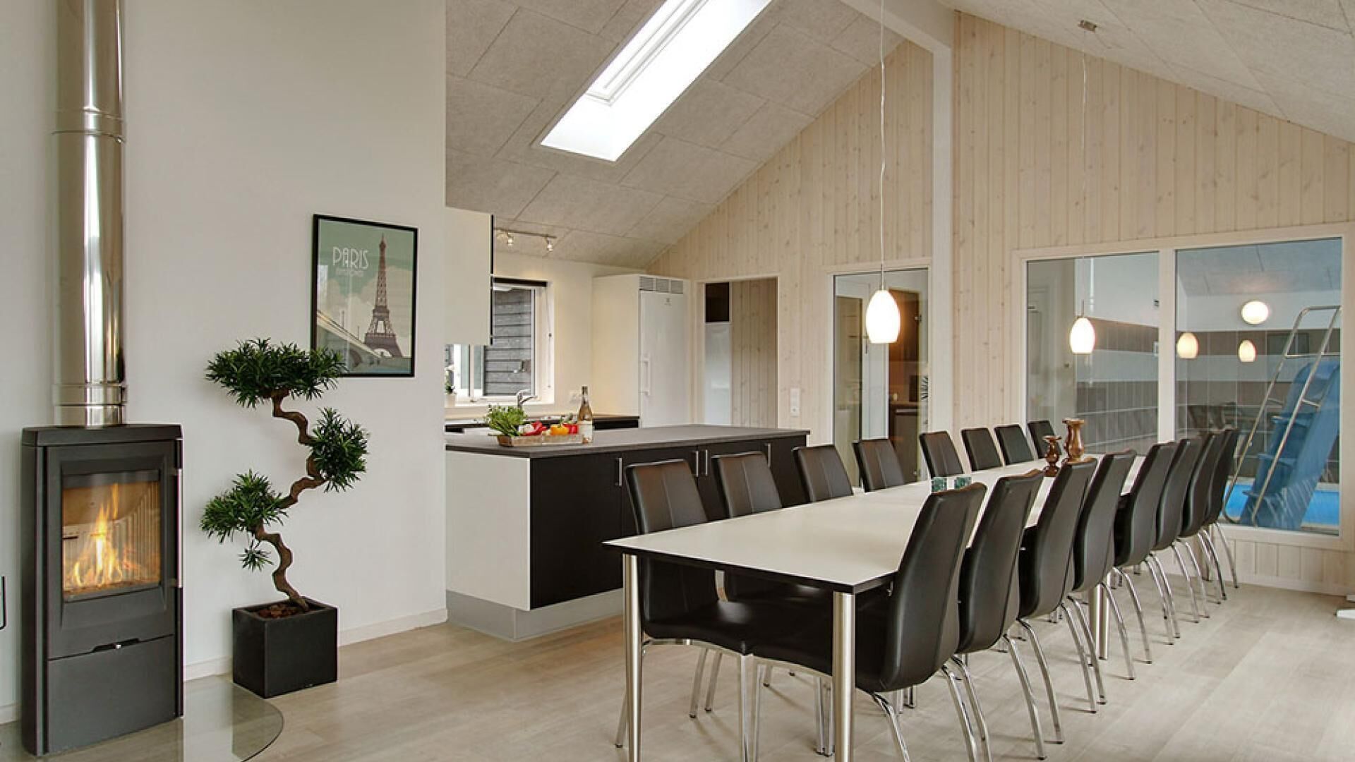 Une cuisine moderne dotée d’un îlot central, d’un coin repas avec une longue table et des chaises, et d’un poêle à bois.