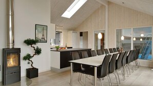 Una cocina moderna con una isla central, una zona de comedor con una mesa grande y sillas, y una estufa de leña.