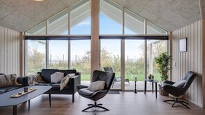 A spacious living room with a large window, a black leather sofa, a coffee table, and a side table with a candle. - VillaVilla 725 - Olpenitz, Deutschland (Kappeln)