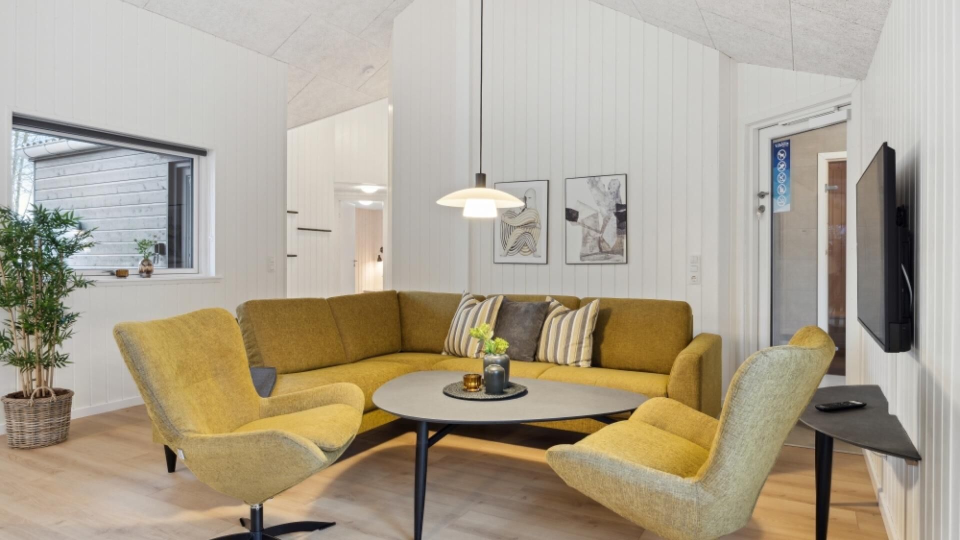 A modern living room with a yellow sectional sofa, a round coffee table, and a TV mounted on the wall.