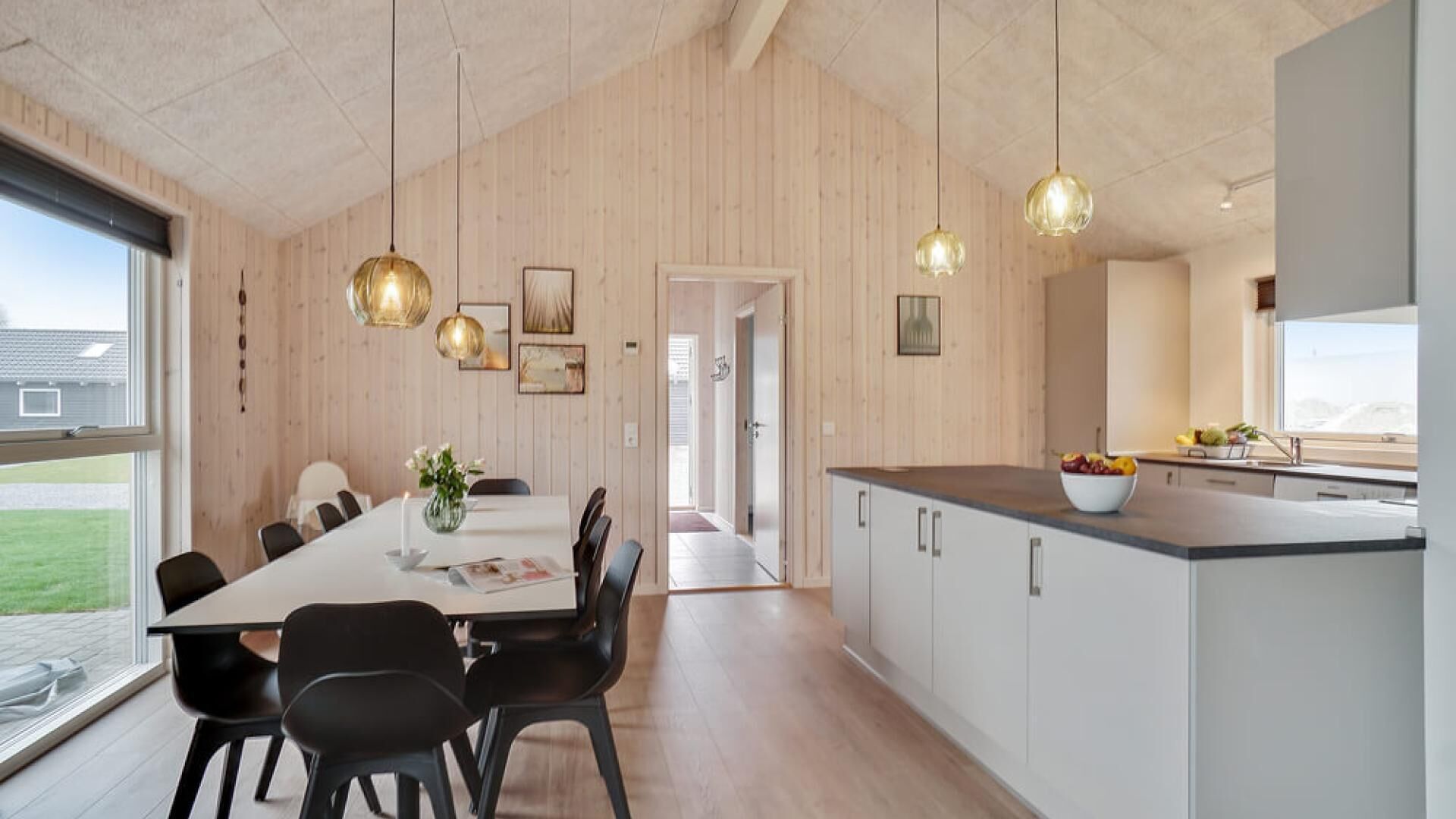 A modern kitchen with a large island, wooden panel walls, and pendant lighting.