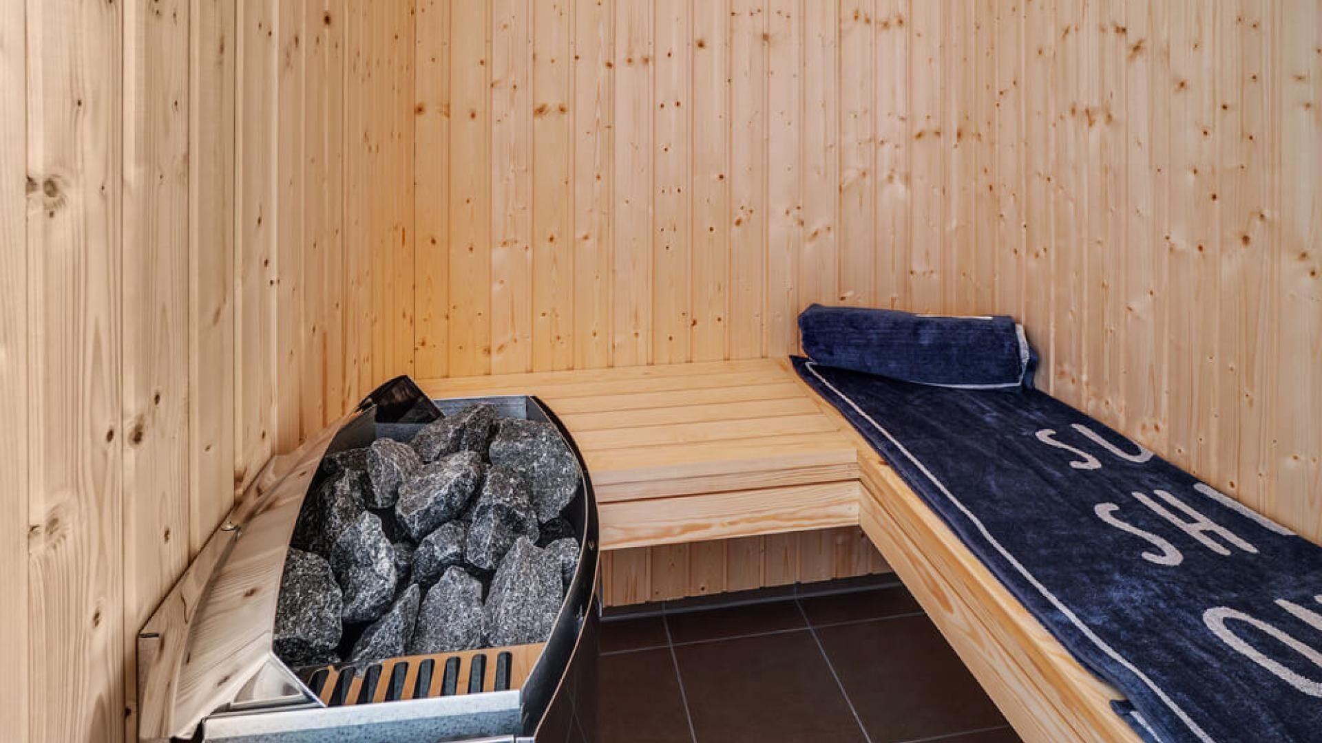 A sauna room with wooden walls, a bench, and a stone heating element.