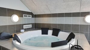 A modern spa room with a large bathtub, black cushioned seating, and two wall-mounted lights. - VillaVilla 708 - Olpenitz, Deutschland (Kappeln)