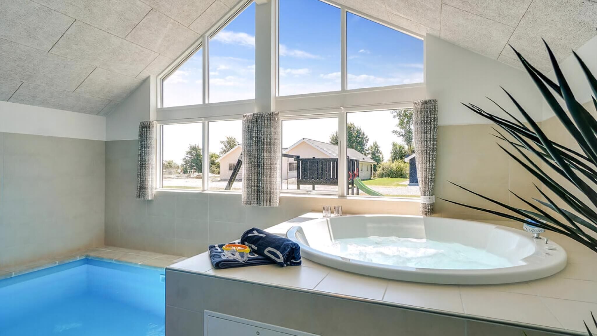A swimming pool with a hot tub, large windows, and a view of a residential area.
