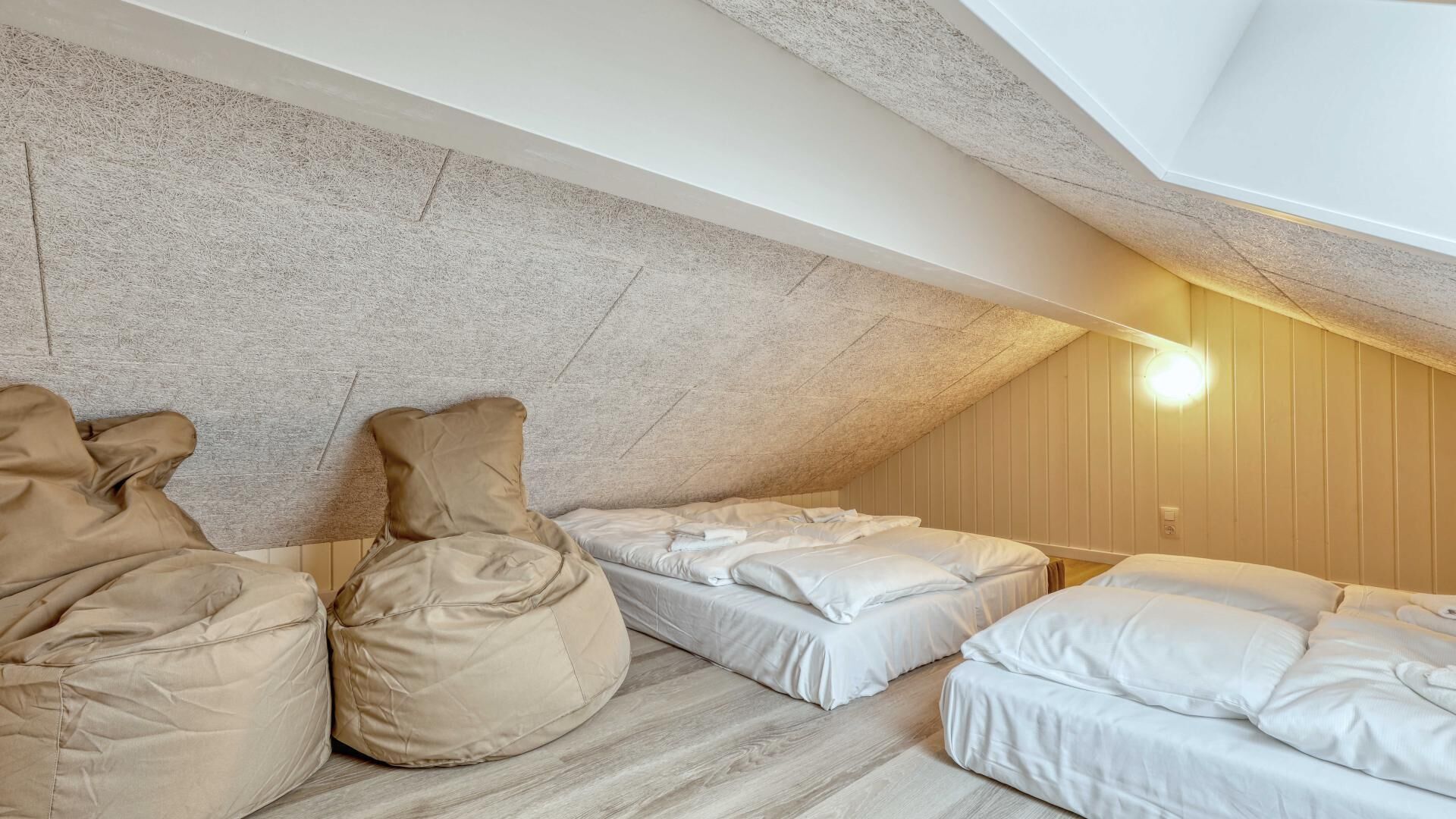 A cozy attic bedroom with three beds, a sloped ceiling, and a wooden wall.